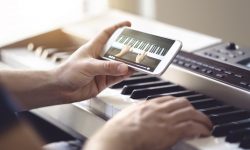 Piano lesson online. Man watching video tutorial with mobile phone and practising playing. Person learning to play an instrument with an internet course and class. Piano lesson online. Man watching video tutorial with mobile phone and practising playing. Person learning to play an instrument with an internet course and class. Pianist training with smartphone.